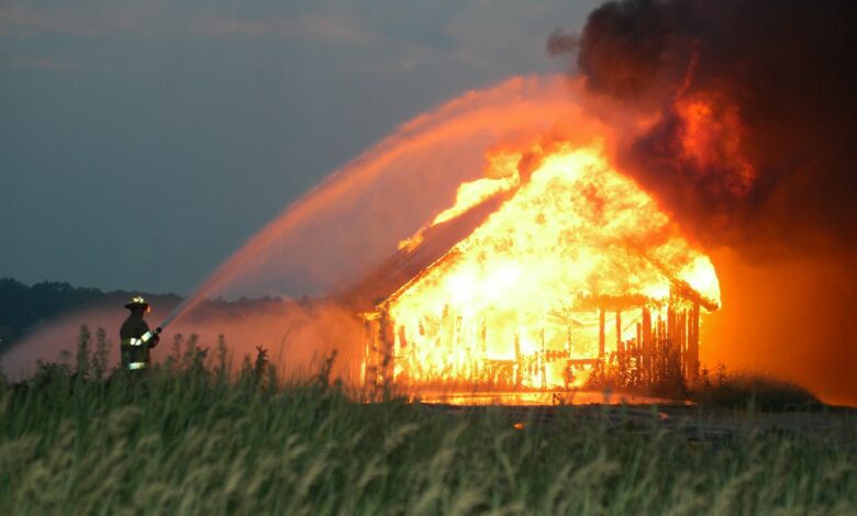firefighter hosing water on burning house