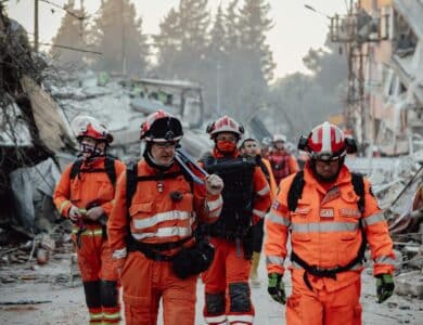 Search and rescue team in orange uniforms in a demolished area, assessing damage and carrying out operations.