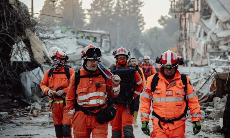 Search and rescue team in orange uniforms in a demolished area, assessing damage and carrying out operations.